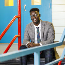 Edmund Adjapong in a gray suit sitting on stairs