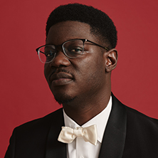 Edmund Adjapong in a gray suit sitting on stairs posing