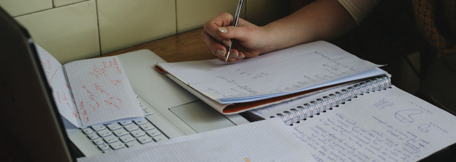 A student studying for an exam taking notes while working on an open laptop. 