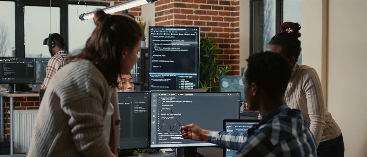 3 IT professionals analyzing code on a monitor. 