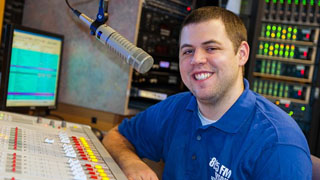Student in blue shirt sitting in front of a microphone and switcher